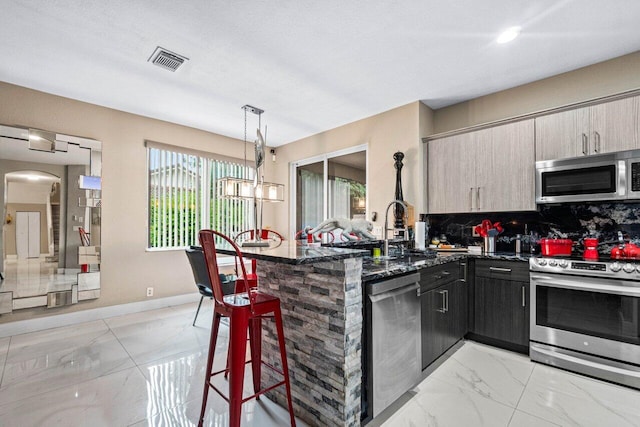 kitchen featuring a kitchen breakfast bar, appliances with stainless steel finishes, tasteful backsplash, a peninsula, and marble finish floor