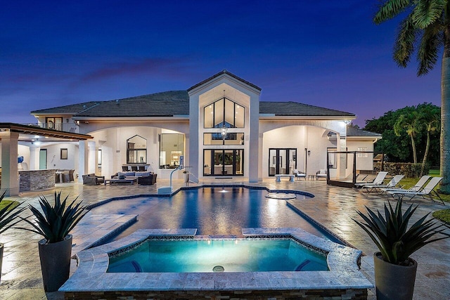 pool at dusk with exterior bar, an in ground hot tub, a patio area, and french doors