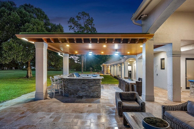 patio at twilight featuring a yard, area for grilling, and exterior kitchen