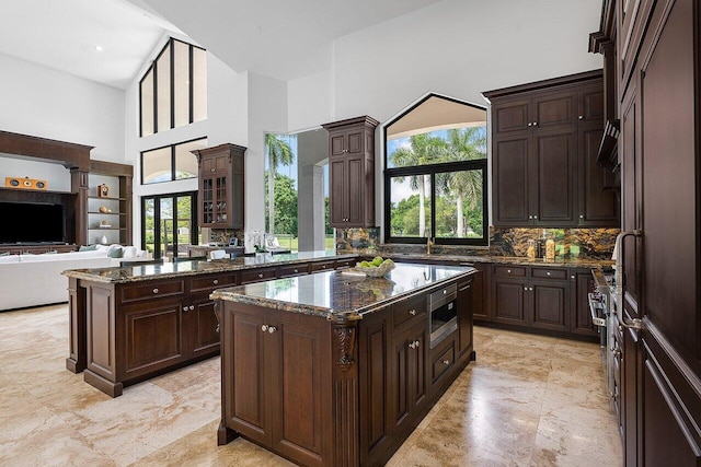 kitchen featuring a high ceiling, a kitchen island, dark brown cabinets, and dark stone countertops