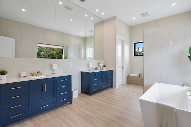 bathroom featuring tile walls, wood-type flooring, vanity, and a bathtub