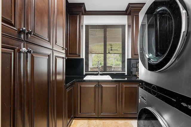 washroom featuring ornamental molding, stacked washer and dryer, sink, and cabinets