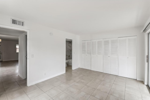 unfurnished bedroom featuring ensuite bath, light tile patterned flooring, and a closet