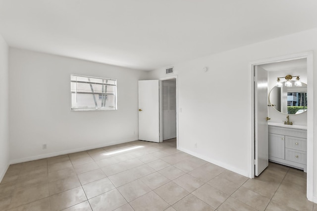 unfurnished bedroom featuring light tile patterned floors, ensuite bathroom, and sink