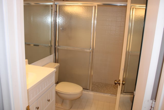 bathroom with tile patterned flooring, vanity, toilet, and a shower with shower door