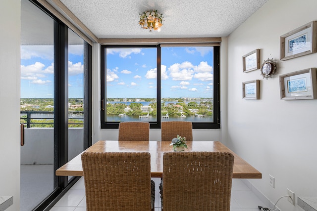 dining room featuring a wealth of natural light, a water view, a textured ceiling, and light tile patterned floors