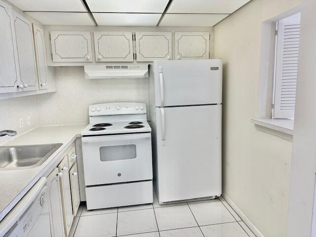 kitchen with light tile patterned flooring, a paneled ceiling, sink, white cabinets, and white appliances