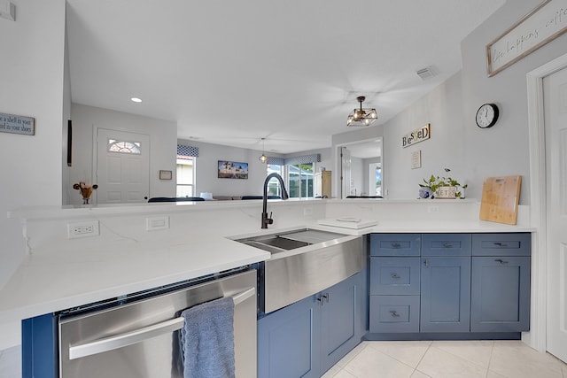 kitchen featuring blue cabinets, sink, stainless steel dishwasher, light tile patterned floors, and kitchen peninsula