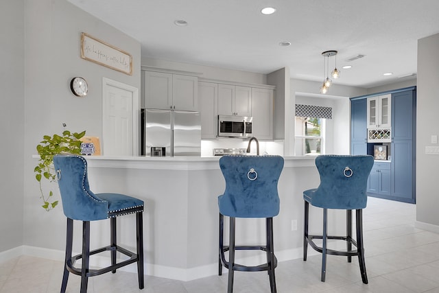 kitchen with a breakfast bar, appliances with stainless steel finishes, hanging light fixtures, and blue cabinetry