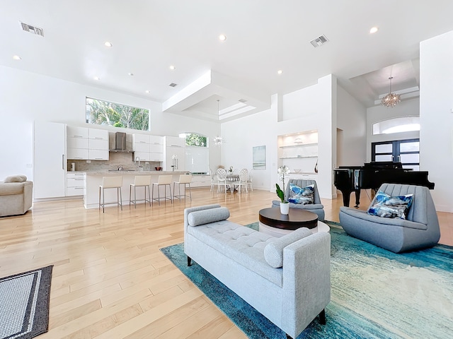 living room featuring sink, an inviting chandelier, light hardwood / wood-style flooring, a high ceiling, and french doors