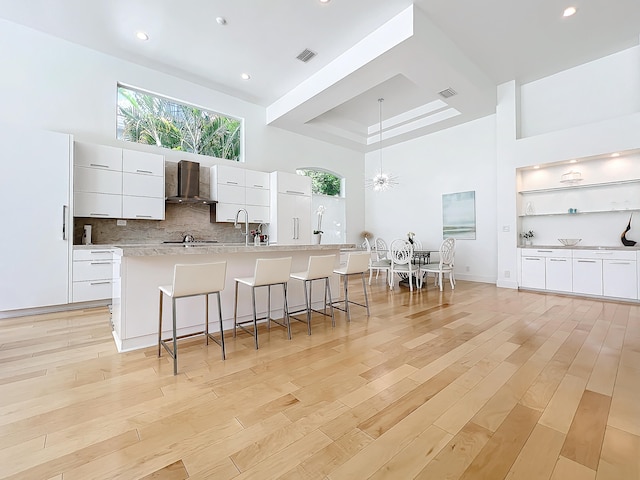 kitchen with wall chimney exhaust hood, white cabinetry, a large island, and light hardwood / wood-style flooring