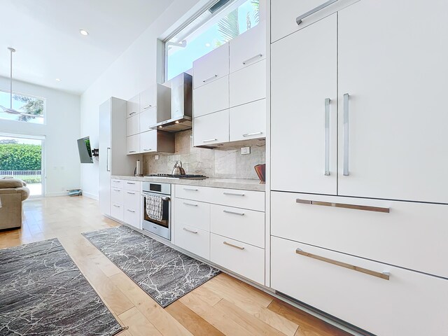 kitchen with white cabinets, light hardwood / wood-style flooring, wall chimney range hood, stainless steel appliances, and a wealth of natural light