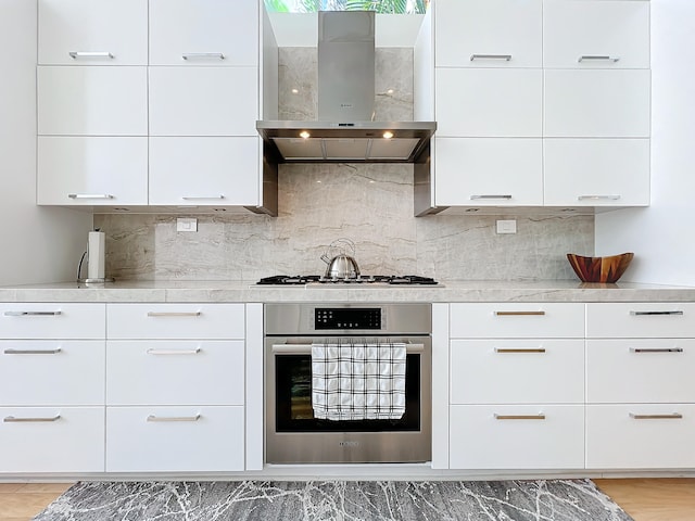 kitchen with appliances with stainless steel finishes, wall chimney range hood, and white cabinets