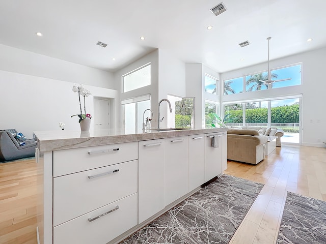 kitchen featuring white cabinetry, a center island with sink, light hardwood / wood-style floors, and a healthy amount of sunlight