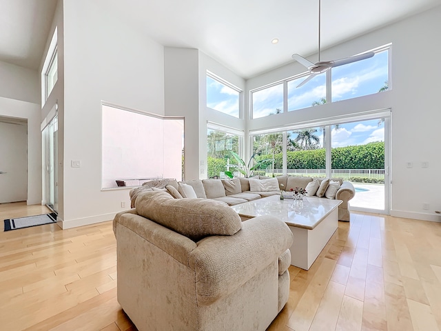 living room featuring a high ceiling, ceiling fan, and light hardwood / wood-style flooring