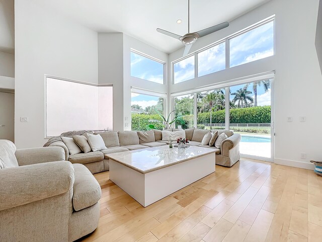 living room featuring ceiling fan, light hardwood / wood-style flooring, plenty of natural light, and a high ceiling