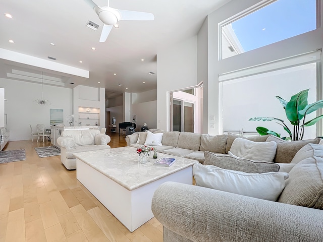 living room with light wood-type flooring, a high ceiling, and ceiling fan