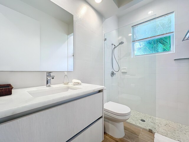 bathroom featuring a tile shower, vanity, toilet, and wood-type flooring