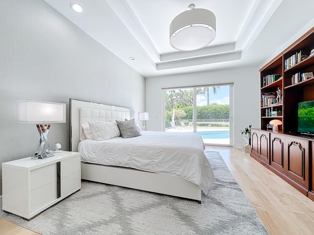 bedroom featuring light wood-type flooring, a tray ceiling, and access to exterior