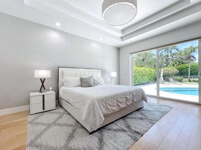 bedroom with light hardwood / wood-style floors, a raised ceiling, and access to outside