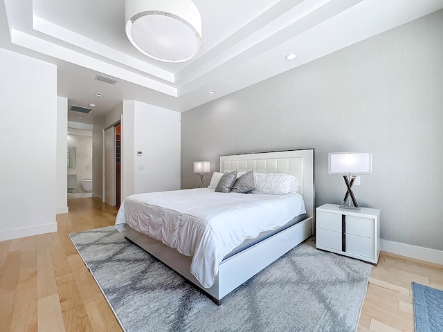 bedroom with wood-type flooring, a closet, a raised ceiling, and ensuite bathroom