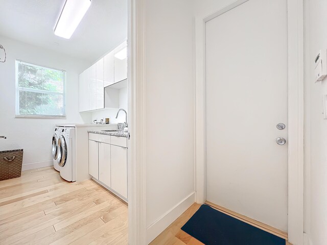 clothes washing area featuring cabinets, light wood-type flooring, washing machine and dryer, and sink