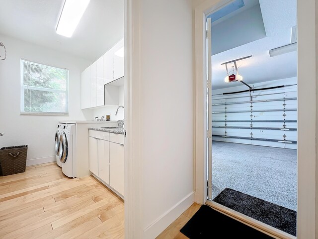 clothes washing area featuring washer and dryer, sink, light hardwood / wood-style flooring, and cabinets