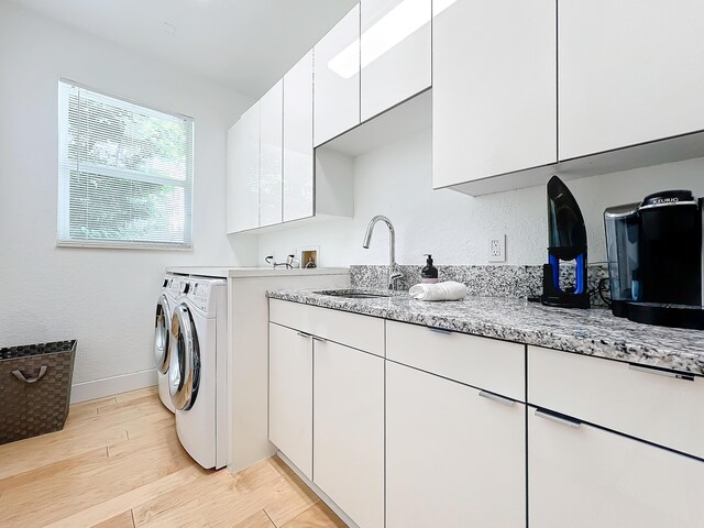 laundry area with cabinets, light hardwood / wood-style floors, sink, and washing machine and clothes dryer