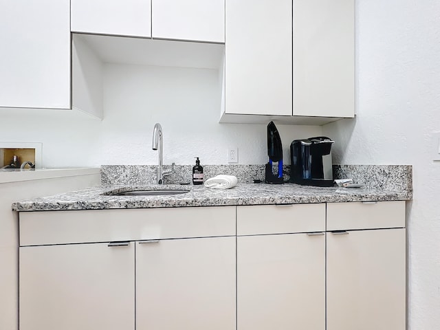 kitchen with white cabinetry, light stone counters, and sink