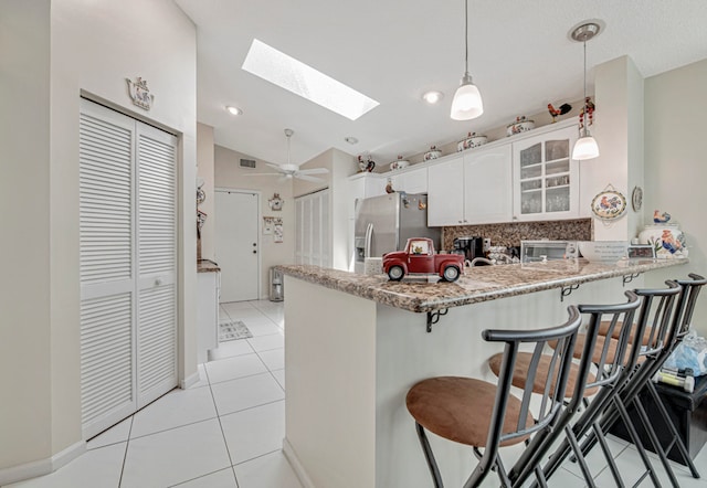 kitchen featuring stainless steel fridge, white cabinets, kitchen peninsula, lofted ceiling with skylight, and ceiling fan