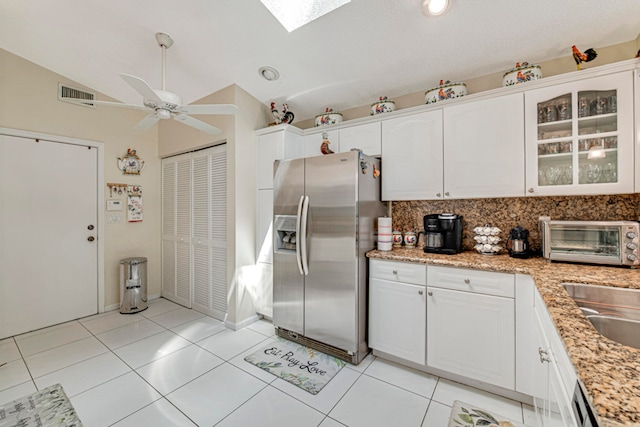 kitchen with vaulted ceiling with skylight, white cabinetry, appliances with stainless steel finishes, light tile patterned floors, and ceiling fan