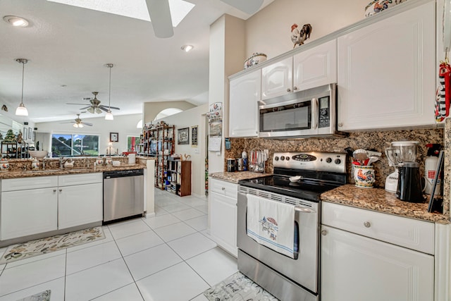 kitchen featuring appliances with stainless steel finishes, white cabinets, pendant lighting, vaulted ceiling with skylight, and ceiling fan