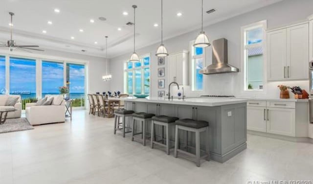 kitchen with an island with sink, ceiling fan, wall chimney exhaust hood, pendant lighting, and a kitchen breakfast bar