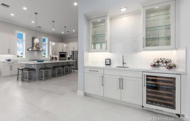 bar featuring wall chimney exhaust hood, a sink, beverage cooler, stainless steel appliances, and backsplash