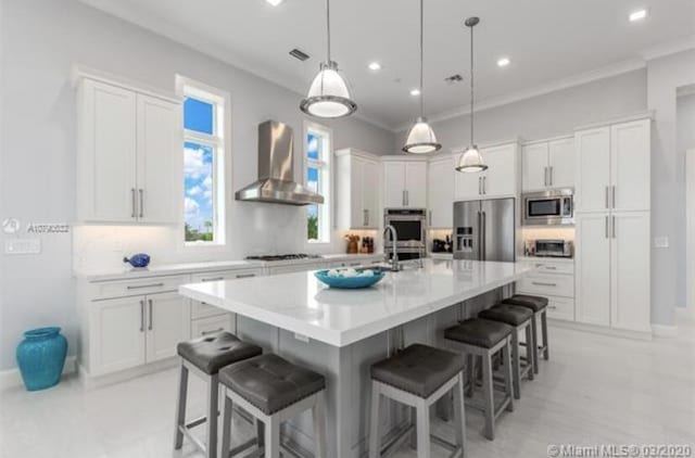 kitchen with ornamental molding, white cabinets, wall chimney exhaust hood, and stainless steel appliances