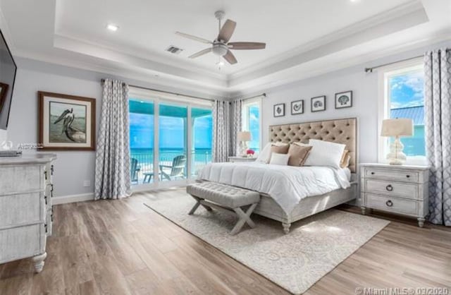 bedroom with access to exterior, a tray ceiling, light wood-type flooring, and ceiling fan