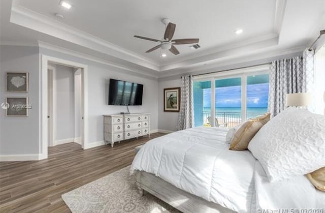 bedroom featuring a tray ceiling, access to exterior, wood finished floors, and baseboards