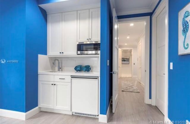 interior space featuring light wood-type flooring, crown molding, sink, dishwasher, and white cabinets