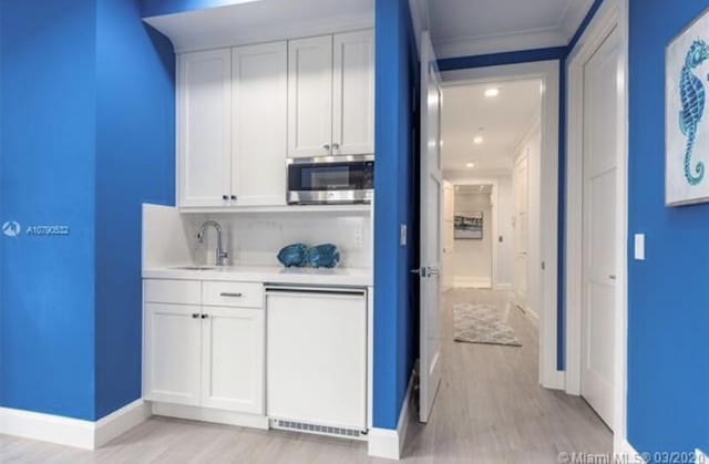 bar with stainless steel microwave, light wood-type flooring, ornamental molding, dishwashing machine, and a sink
