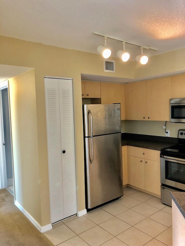 kitchen with light tile patterned floors, a textured ceiling, light brown cabinetry, and stainless steel appliances