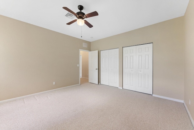 unfurnished bedroom featuring carpet, ceiling fan, and multiple closets