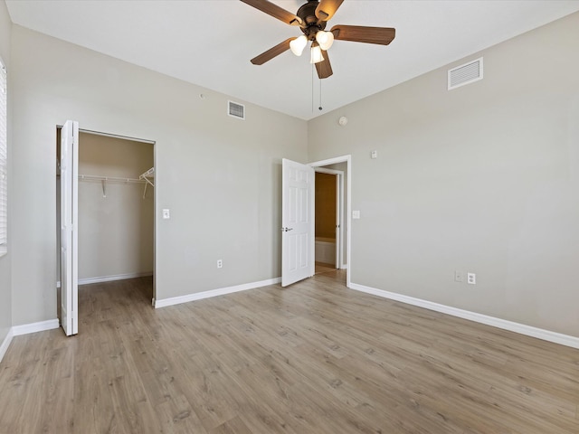 unfurnished bedroom featuring ceiling fan, a closet, a walk in closet, and light hardwood / wood-style flooring