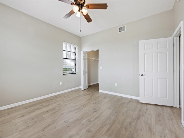 unfurnished bedroom with a walk in closet, light wood-type flooring, a closet, and ceiling fan