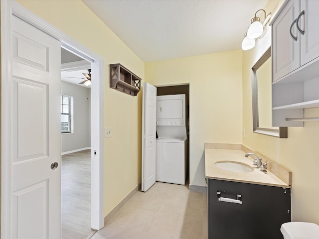 bathroom featuring ceiling fan, stacked washing maching and dryer, a textured ceiling, and vanity