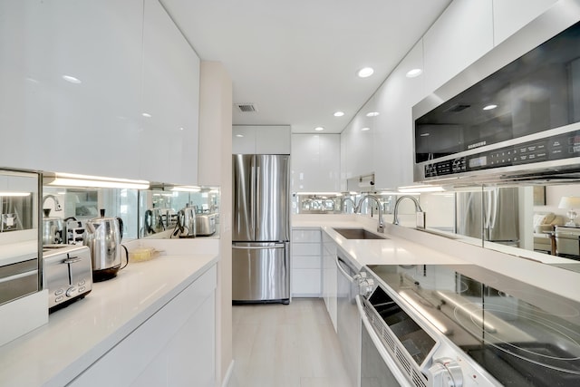 kitchen with appliances with stainless steel finishes, light hardwood / wood-style flooring, sink, and white cabinets