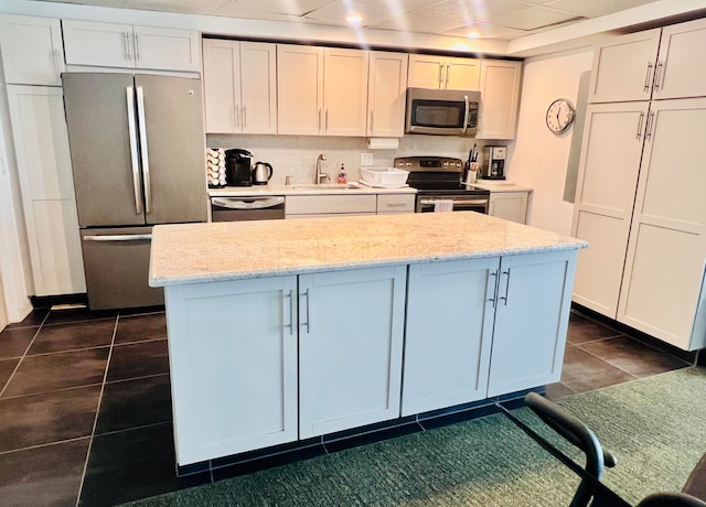 kitchen with dark tile patterned floors, stainless steel appliances, sink, white cabinetry, and light stone counters