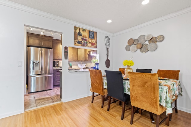 dining room featuring ornamental molding, a textured ceiling, and light hardwood / wood-style flooring