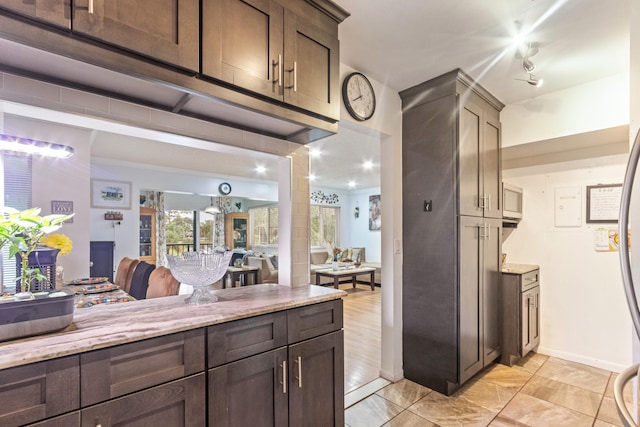 kitchen featuring light tile patterned floors, crown molding, light stone counters, and dark brown cabinetry