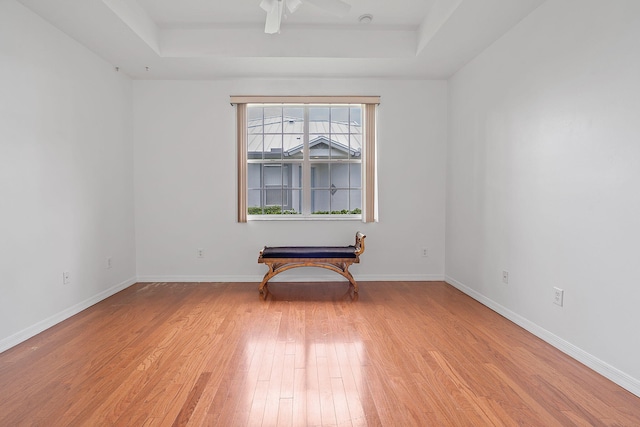 unfurnished room with ceiling fan, light wood-type flooring, and a tray ceiling