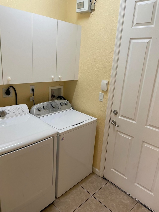 clothes washing area featuring cabinets, light tile patterned flooring, and washing machine and dryer